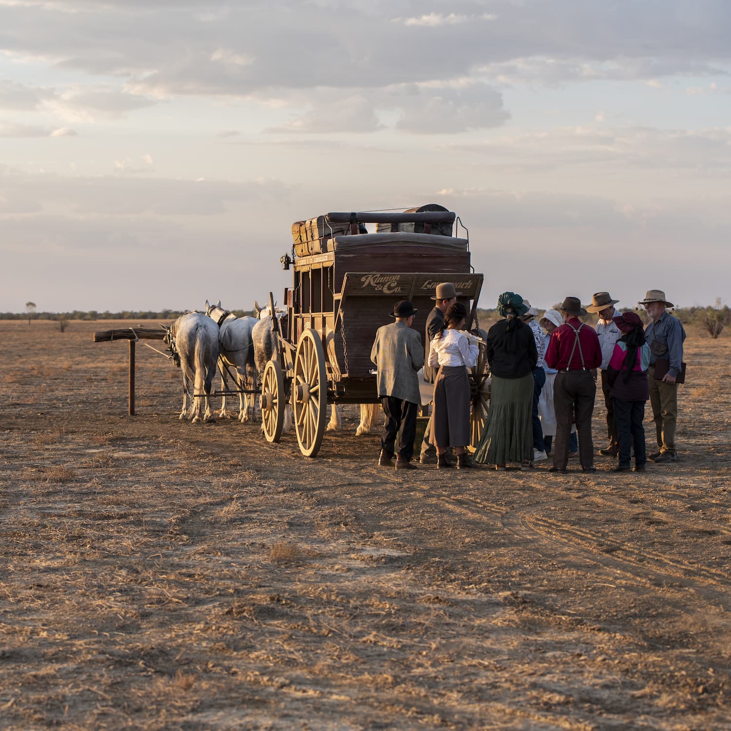 Guests enjoying traditional refreshments at the back of the Cobb and Co Stagecoach, as the sun does down across the Longreach Common