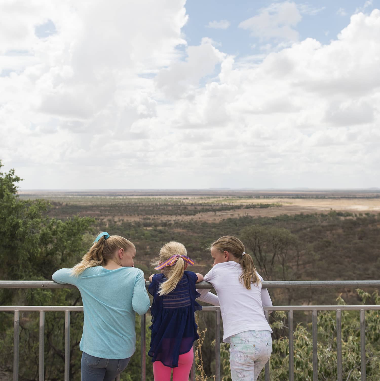 Three young girls at Australian Age of Dinosaurs museum, Winton, leaning on the railing overlooking the outback landscape