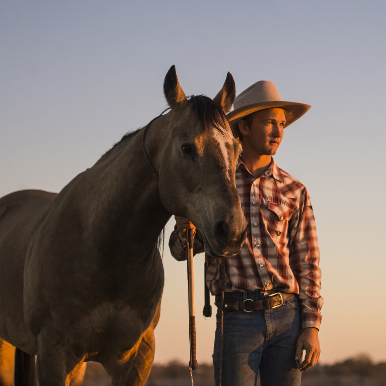 Closeup of Lane Kinnon standing next to his horse at sunset