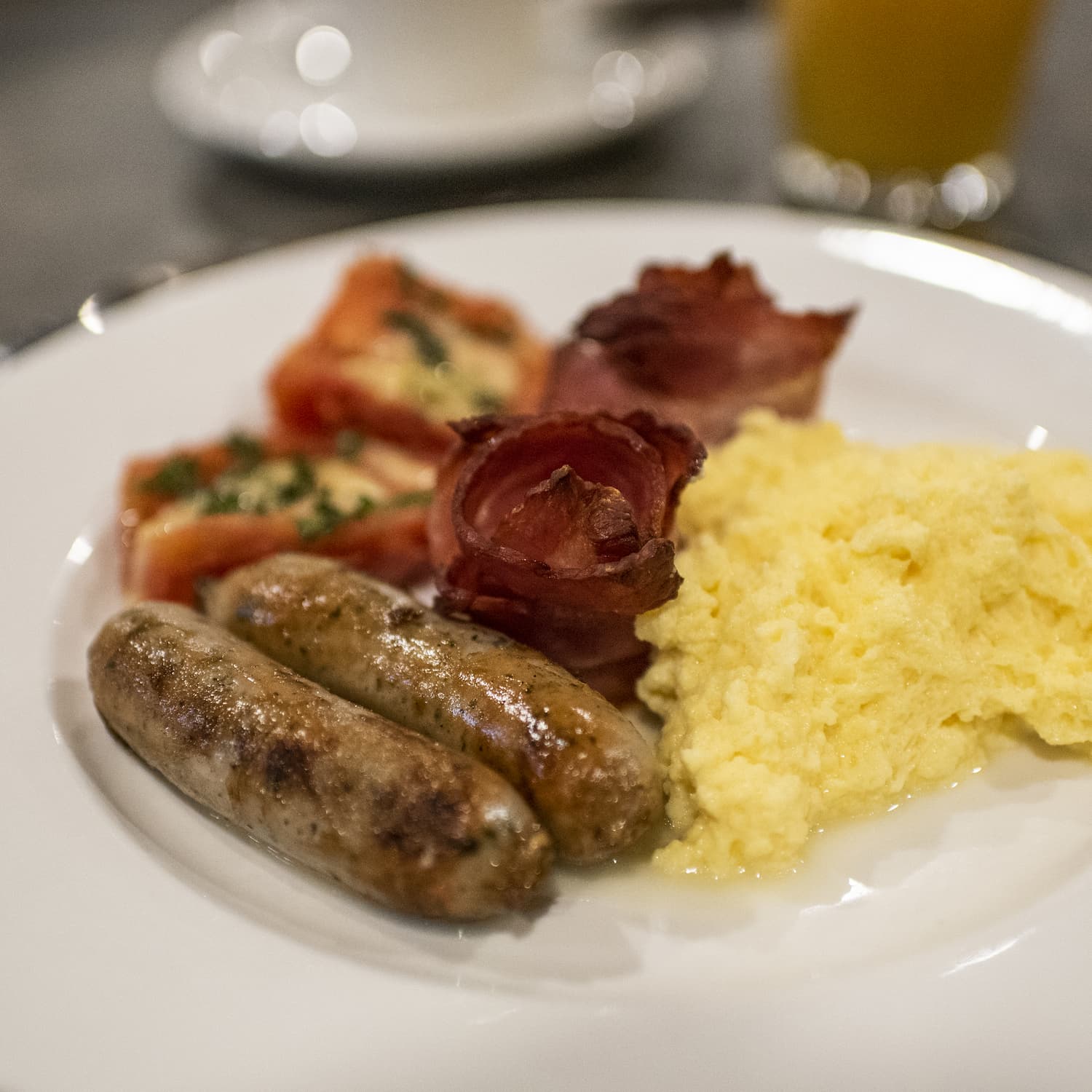 Plate with cooked sausages, grilled tomatoes, bacon and scrambled eggs