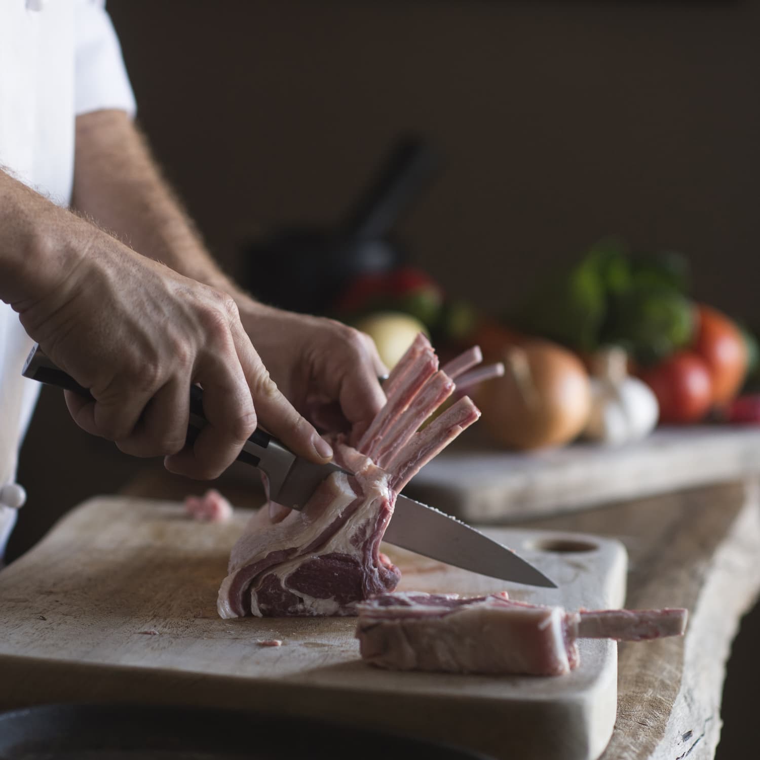 Chef cutting lamb chops on timber board