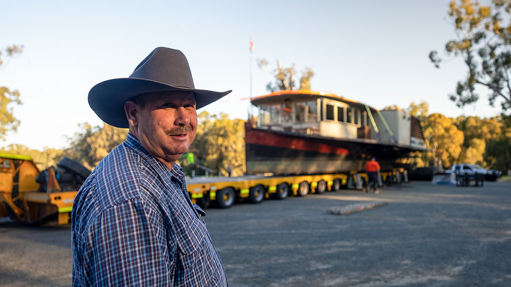 Richard Kinnon looking into the camera, standing in front of the Pride of the Murray as it is loaded onto a vehicle