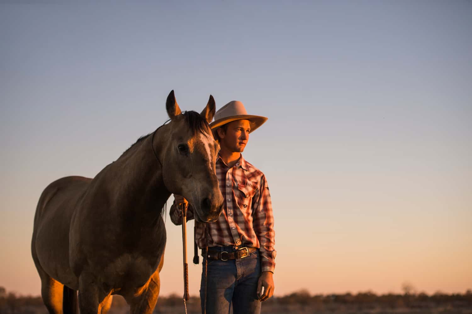 A stockman standing with his horse at sunset