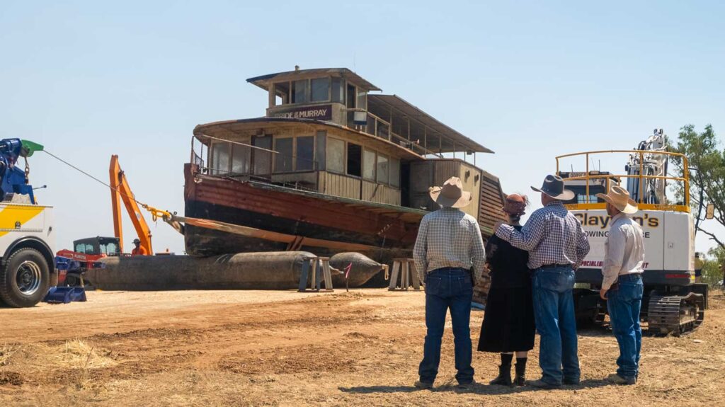 The Pride of the Murray paddlewheeler on a riverbank hardstand with for family members looking on