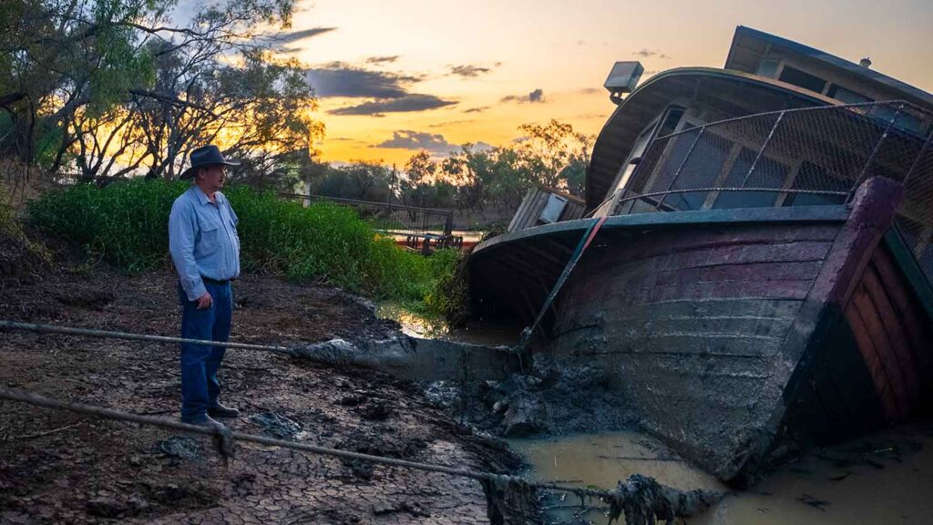 Richard Kinnon stands on the banks of the Thomson River at susnet, looking over the partly retrieved Pride of the Murray paddlewheeler