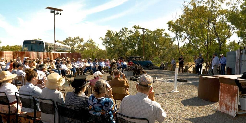 Crowd of people sitting in a semi-circle outside listening to an announcement