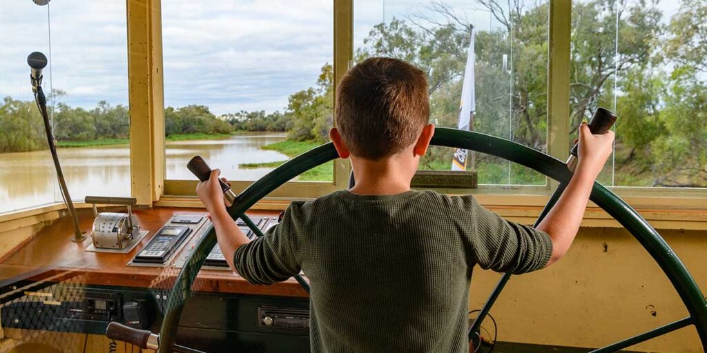 A young boy in the wheelhouse of the Pride of the Murray, holding the wheel