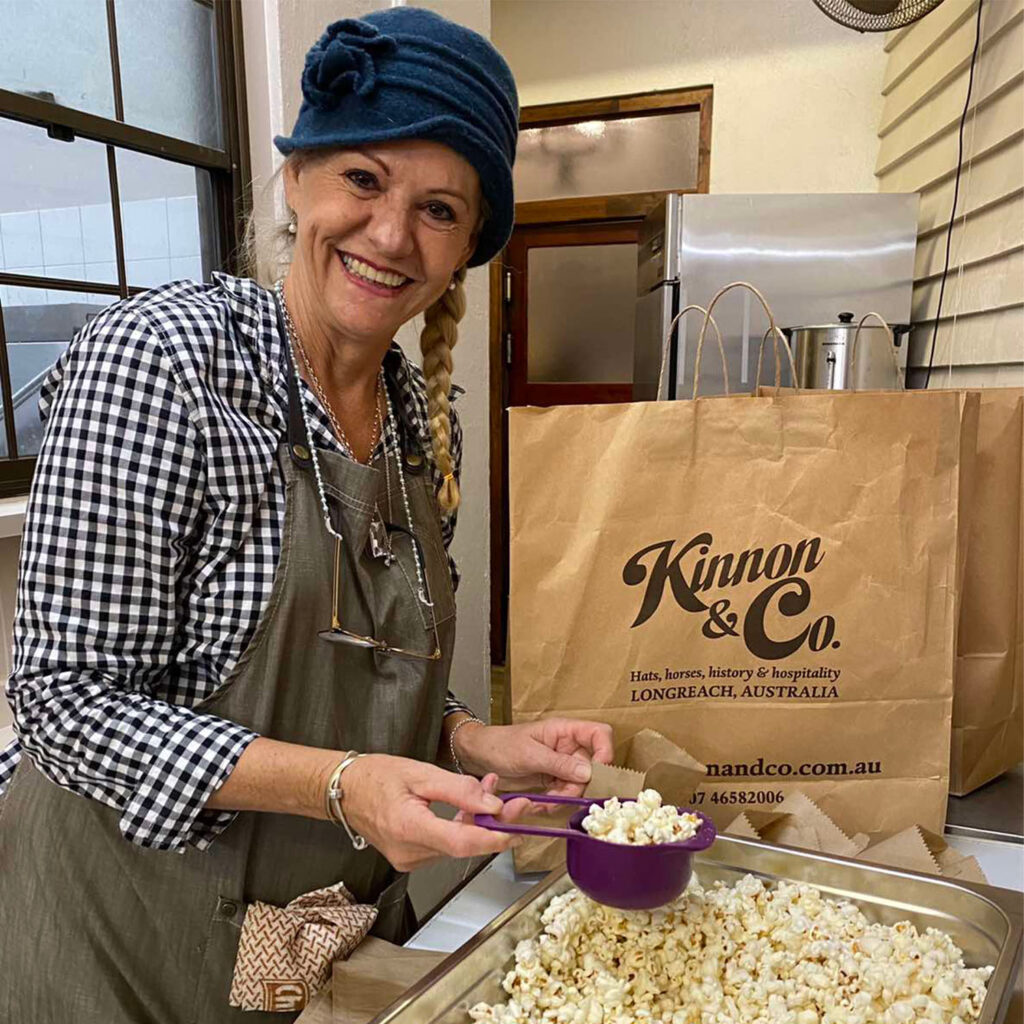 A woman scooping popcorn standing in front of a Kinnon & Co paper bag