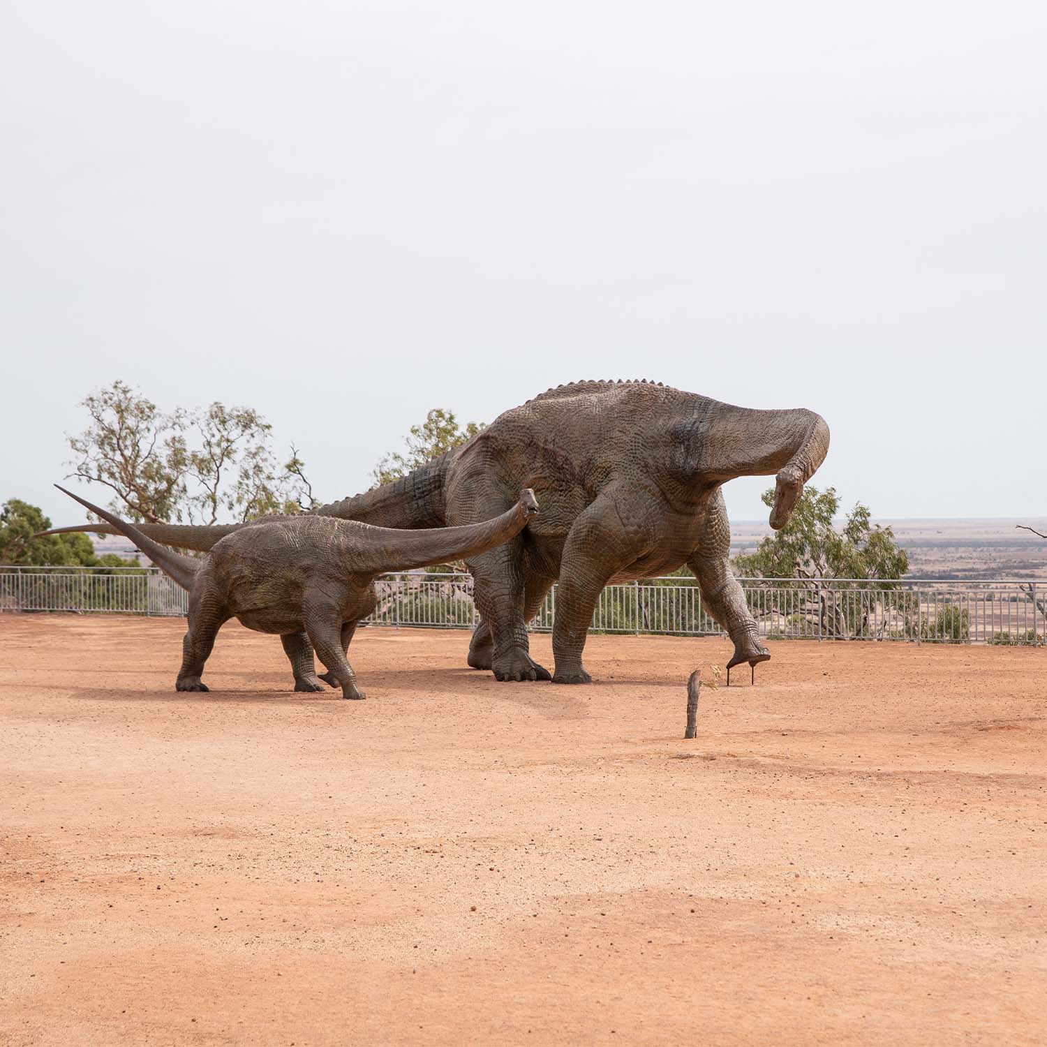 Two dinosaur statues in front of a low fence