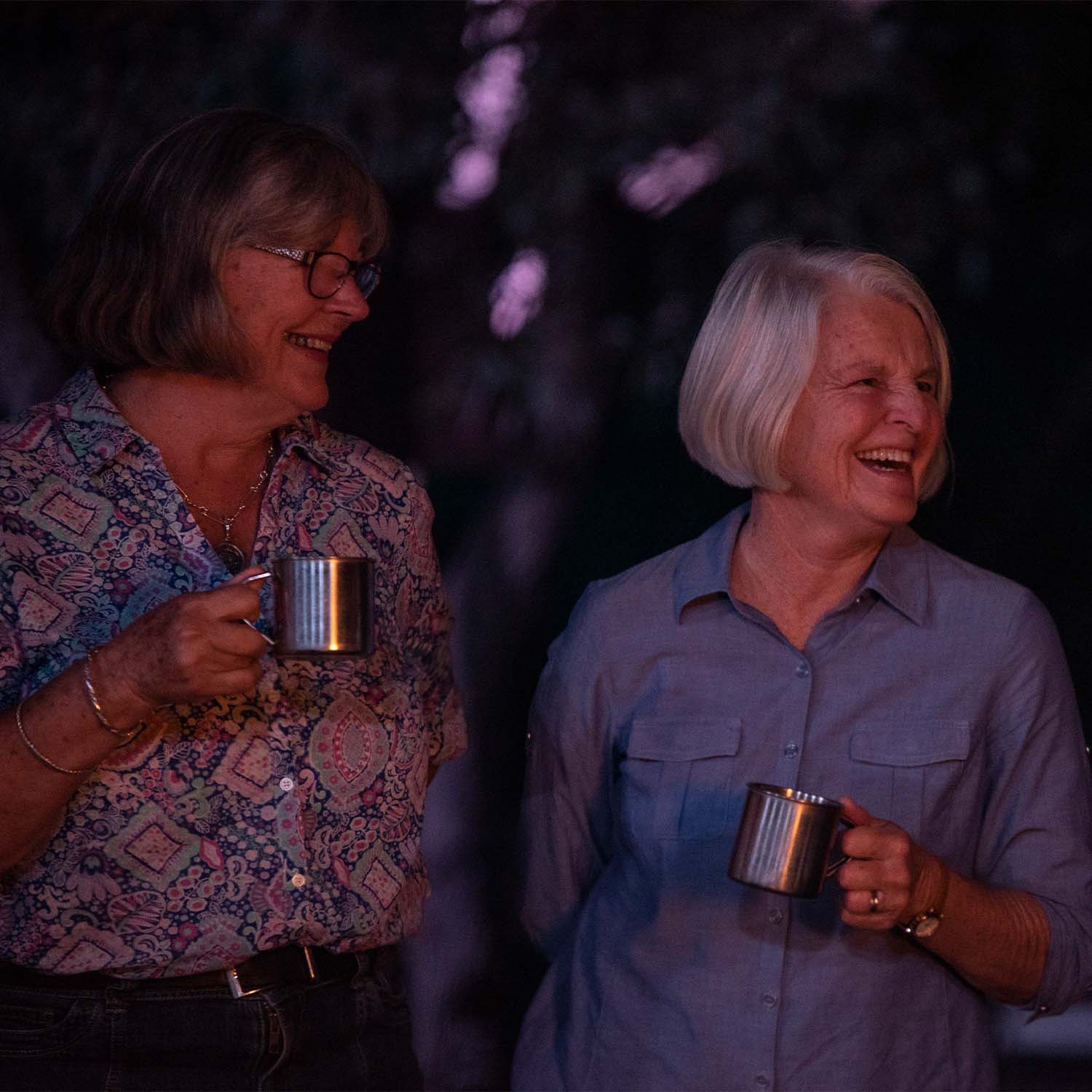 Two women looking off to the side holding metallic cups at night