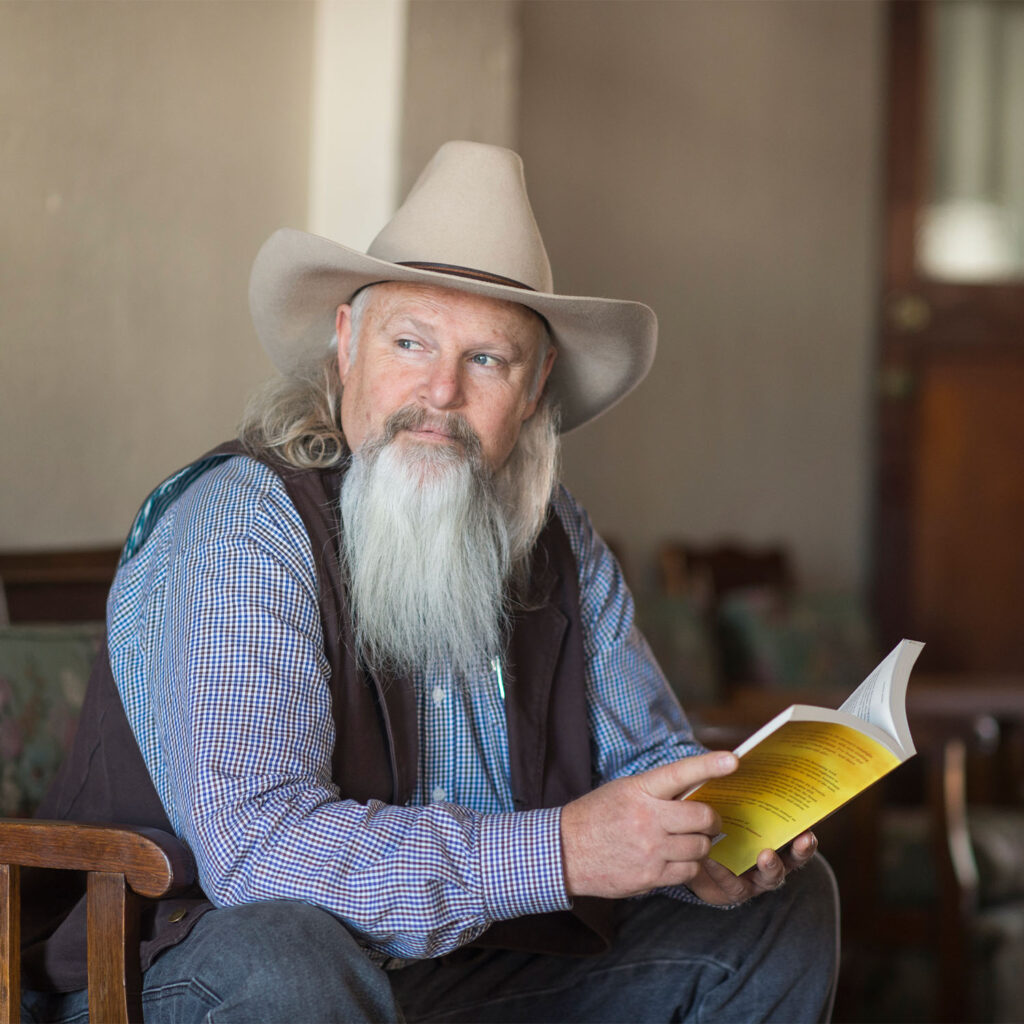 A man sitting, holding a book and looking into the distance