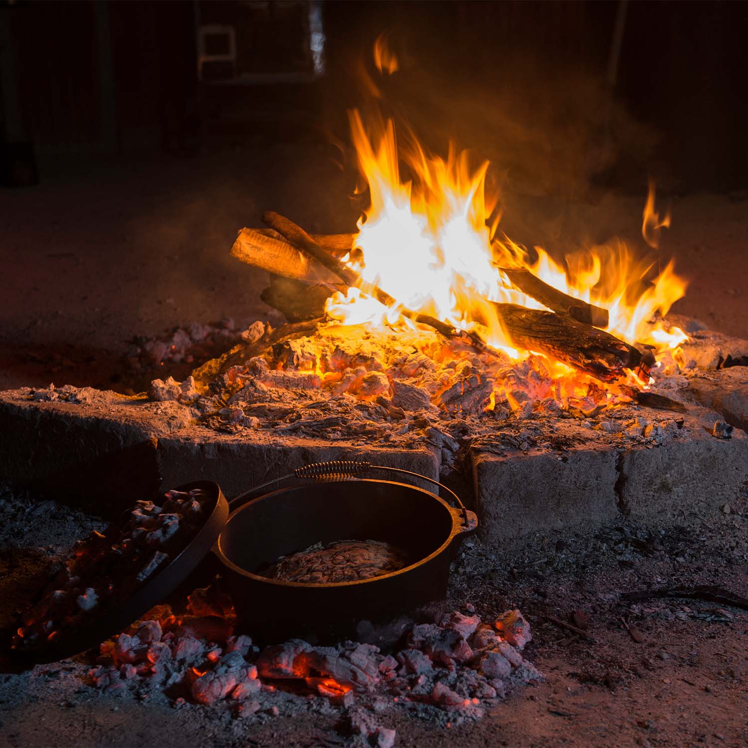 A cast-iron pan sat beside a flaming campfire