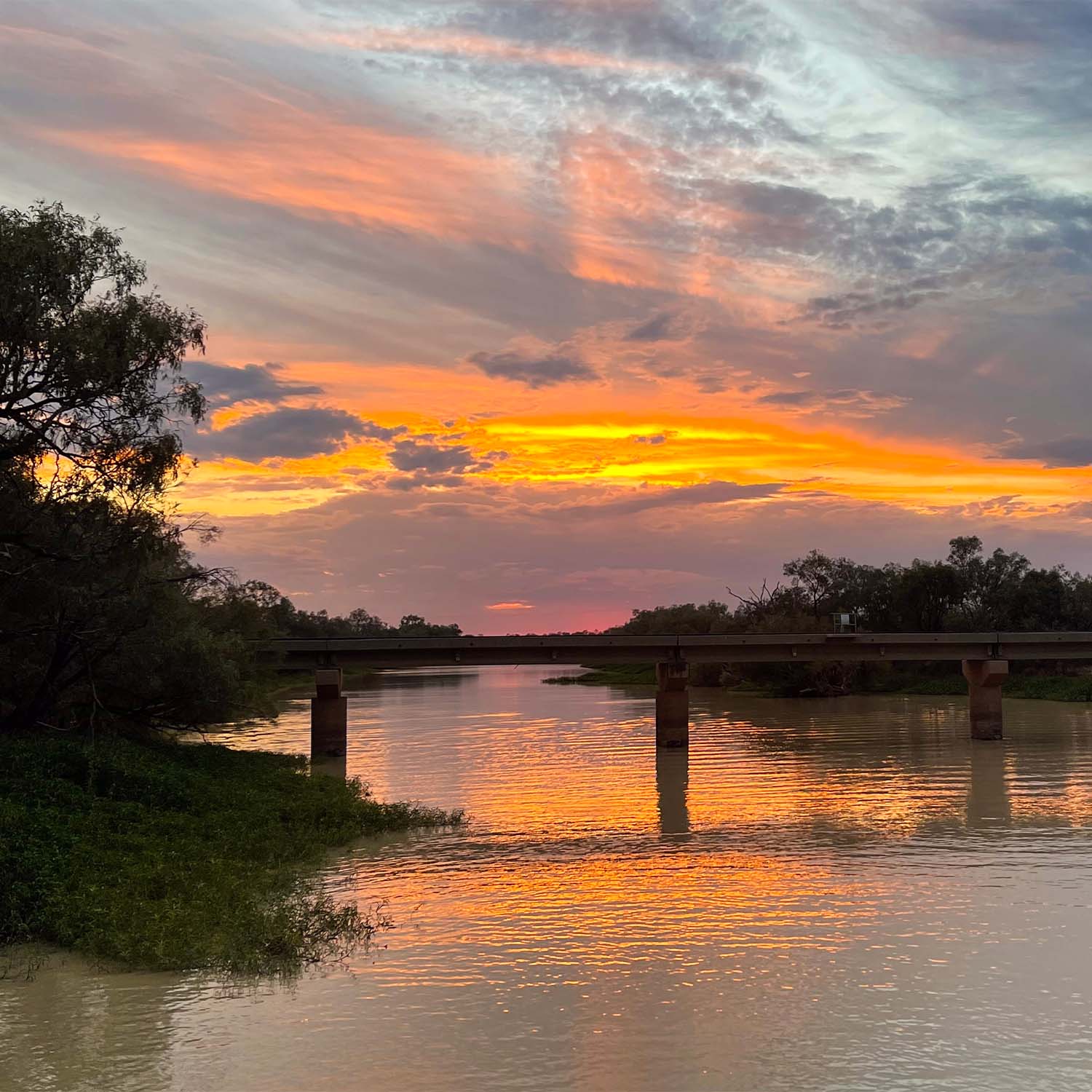 The silhouette of a bridge crossing the Thomson with the sunset in the background