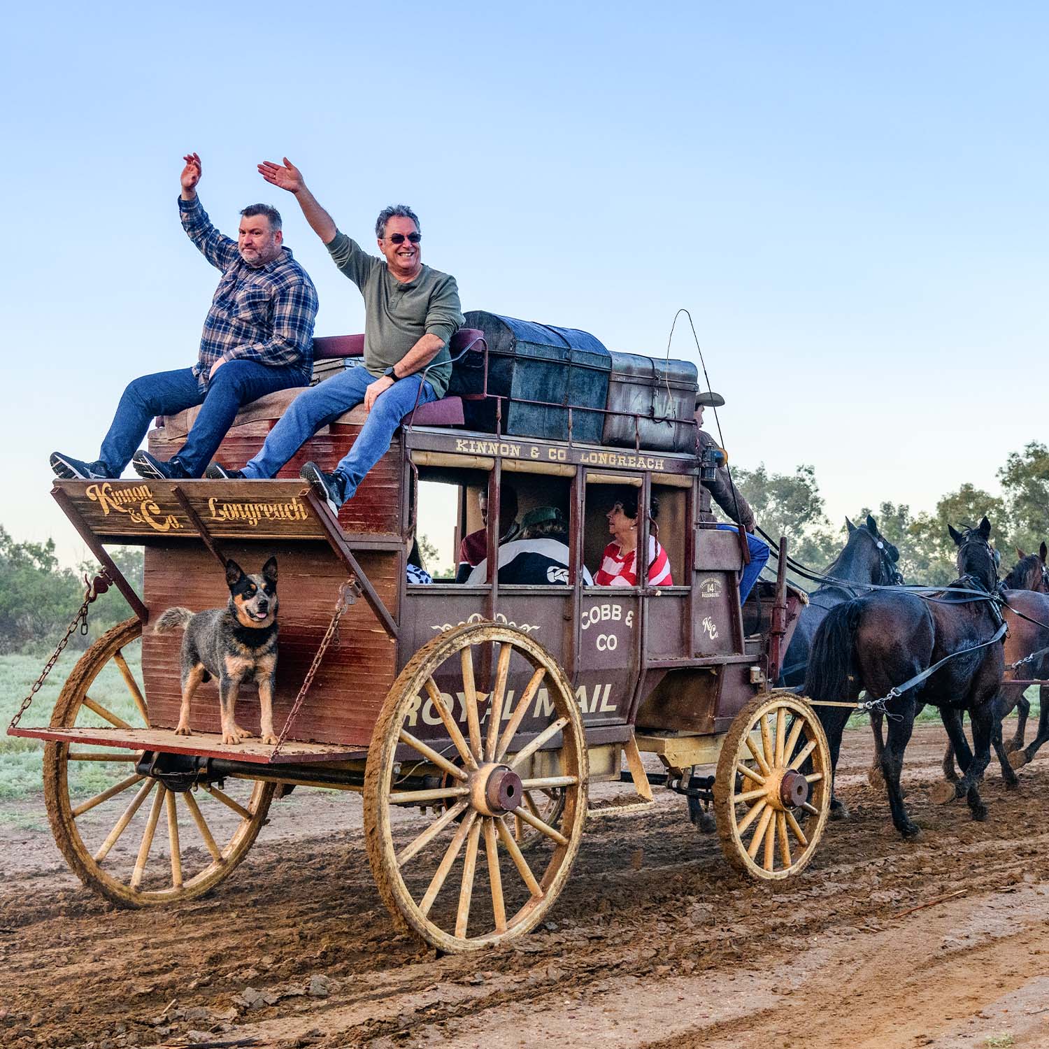 Two men waving atop the cobb & co stagecoach on a muddy track